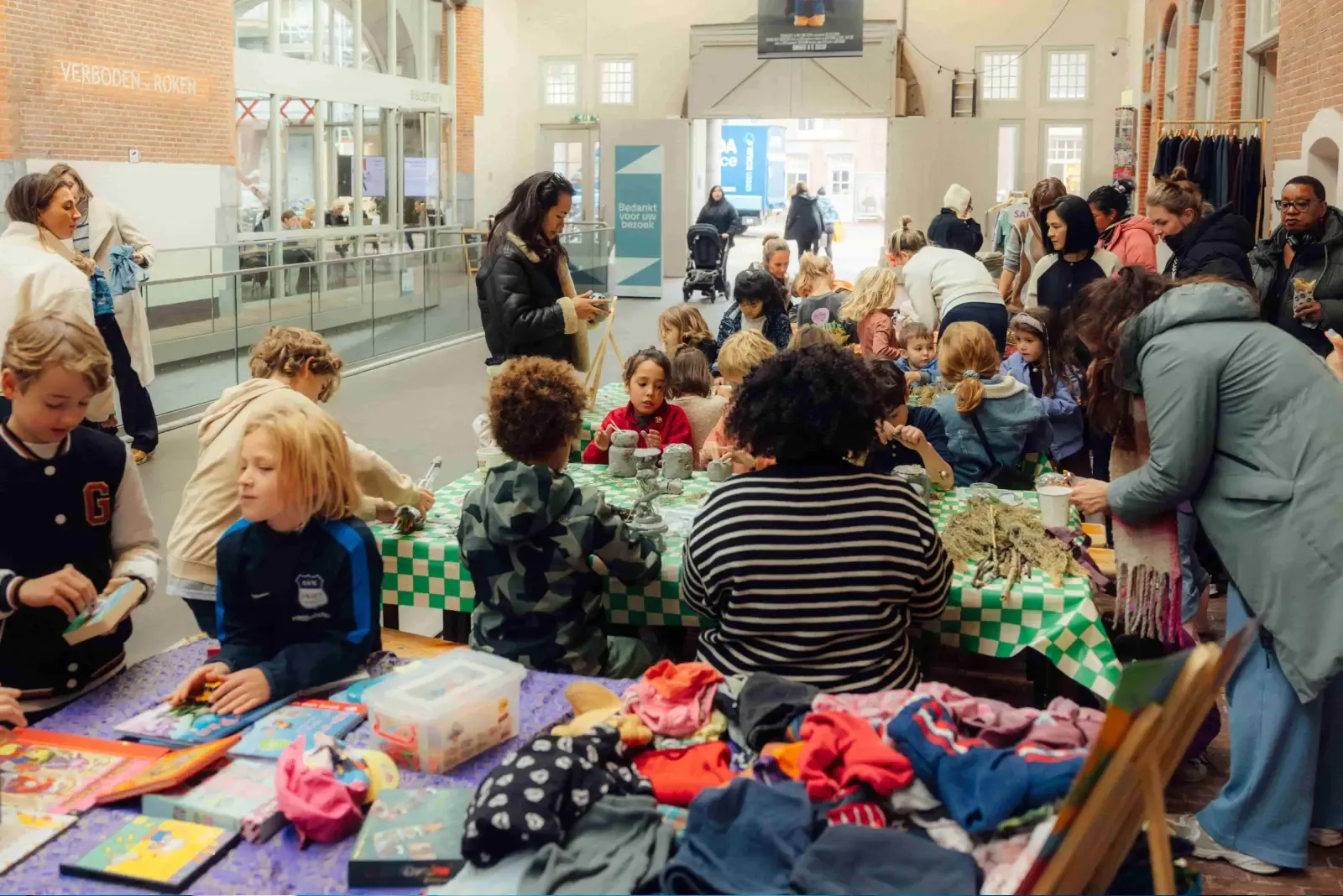 Kinderen en ouders knutselen samen aan een lange tafel in De Hallen