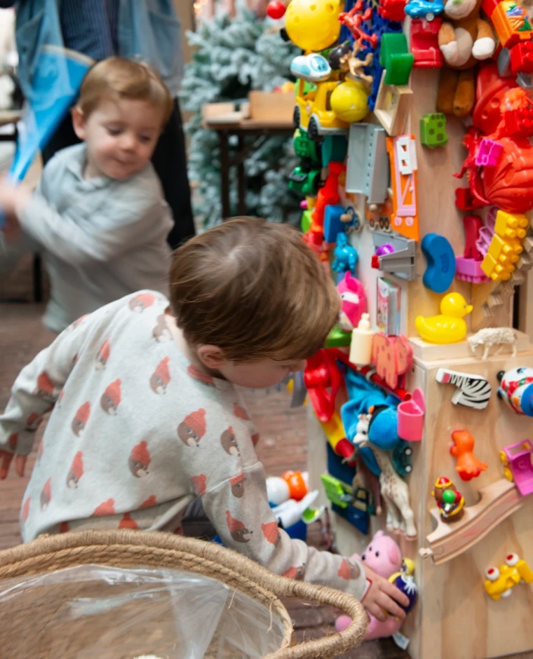 Twee jongens hangen speelgoed op aan een houten pilaar