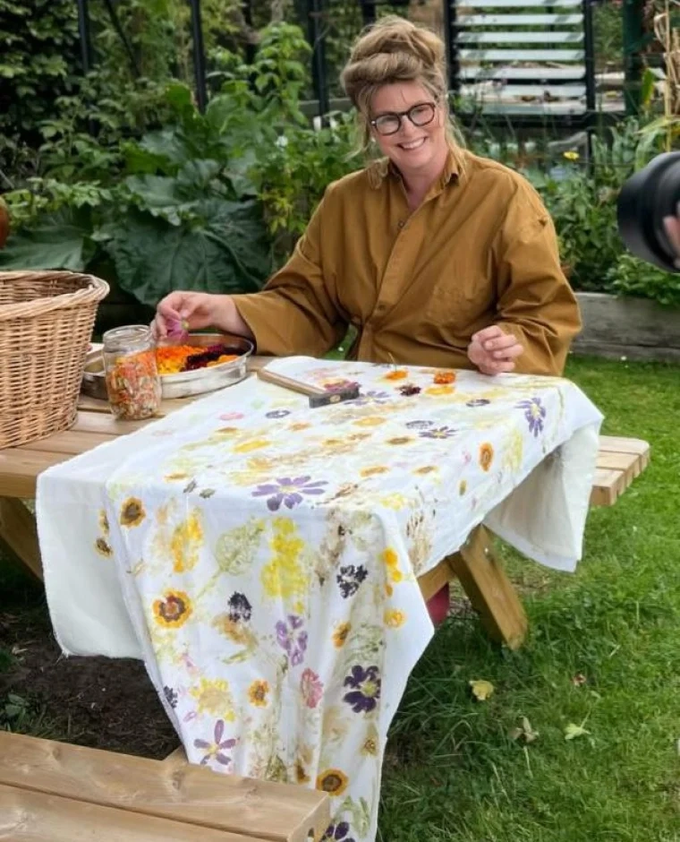 Marte van Studio Marte aan een picknicktafel in de tuin met een textielkleed vol afdrukken van bloemen