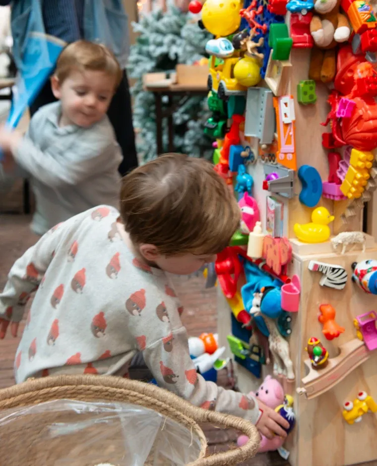 Twee jongens zoeken speelgoed uit aan een houten zuil vol kleurrijk ruilspeelgoed