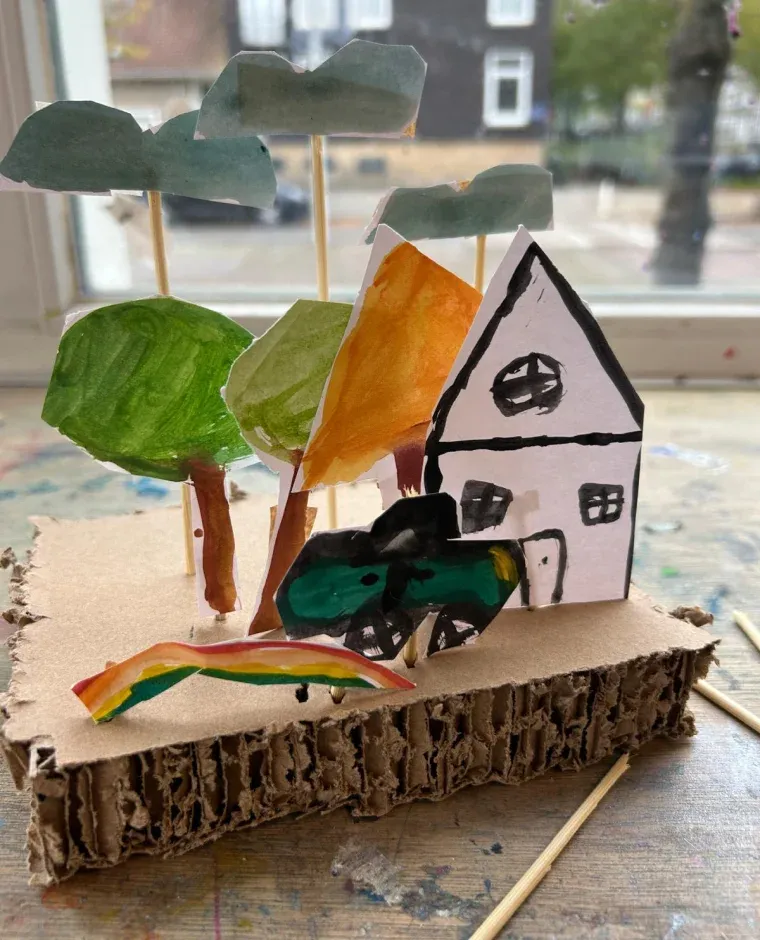 Knutsellandschap van karton met geschilderde bomen, een huisje en een regenboog, gemaakt door een kind tijdens de workshop