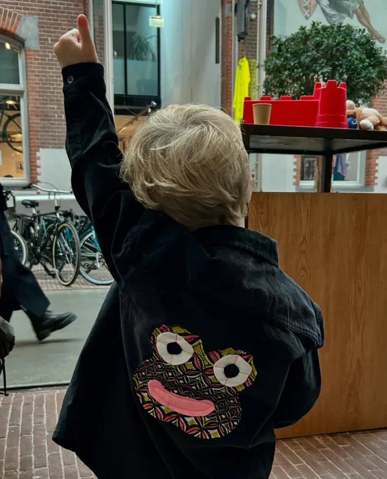 Jongen draagt een zwarte spijkerjas met een kikker gemaakt van kleurrijke lappen stof